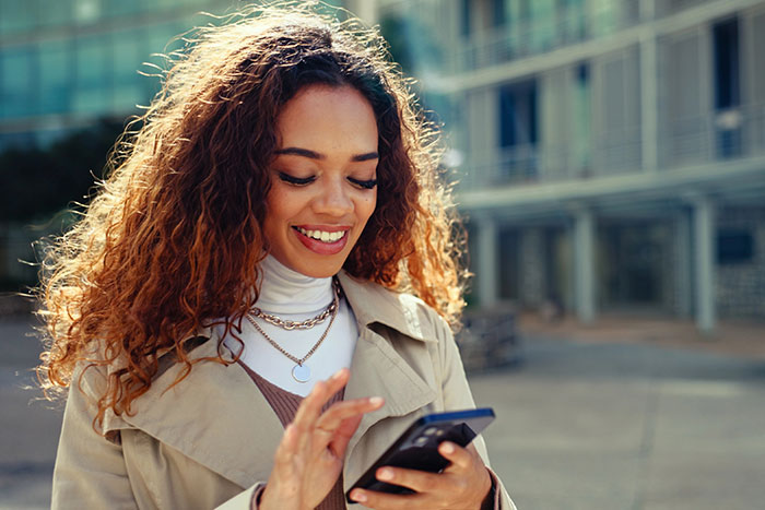 Image of a woman using her phone, smiling.