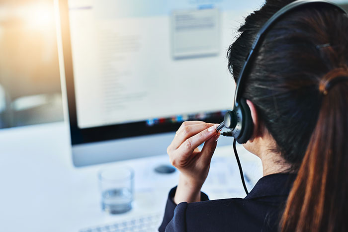 A woman with a headset at her computer delivers customer service, showcasing her commitment to enhancing customer experiences.