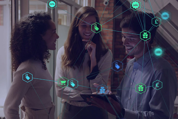 Three people discussing while looking at a tablet, overlaid with digital network icons representing communication, shopping, and finance.