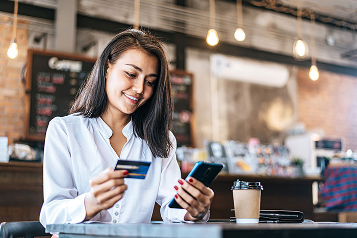 Photo of a woman at a coffee shop, using her credit card to pay for her order.
