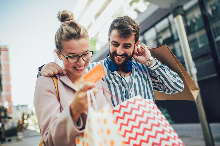 A happy couple with shopping bags and a credit card on a city street.